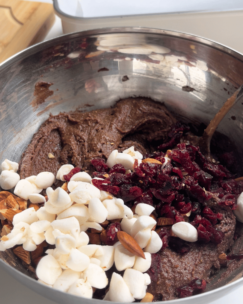 chocolate fudge in a metal bowl with marshmallows, almonds, and cranberries chopped on top