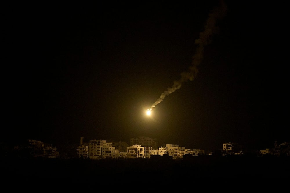 An Israeli army flare drifts over buildings destroyed during the Israeli ground and air operations in the northern Gaza Strip, as seen from southern occupied Palestine, Monday, September 15, 2025 (AP)