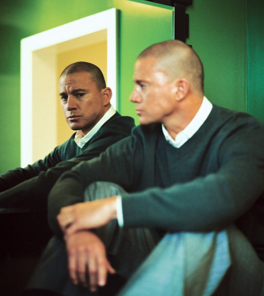 In a room with green walls and a white door frame, Tatum sits next to a mirror that reflects his face.