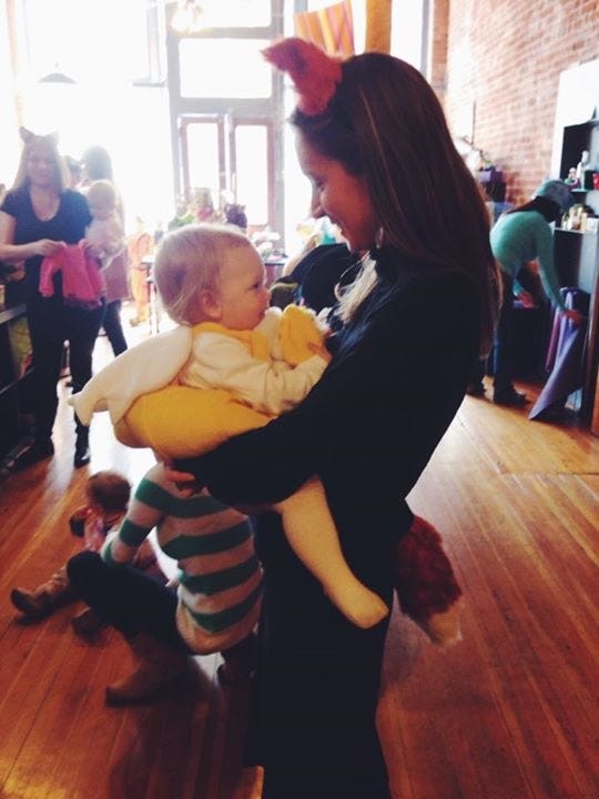 Kari, dressed in all black with fox ears and tail holds a baby dressed in a duck costume