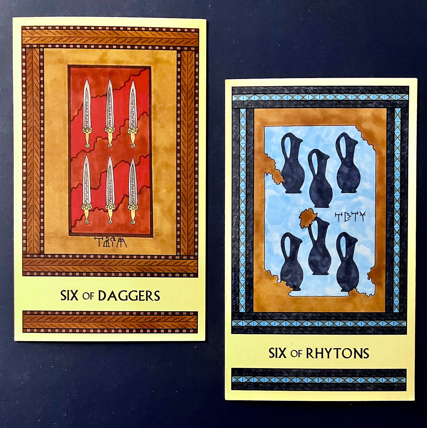 Two Minoan Tarot cards side by side on a midnight blue background. The Six of Daggers, on the left, is painted in shades of deep red, tan, and brown. It shows six fancy engraved daggers laid out in a box lined with luxurious fabric. The Six of Rhytons, on the right, is painted in shades of blue and tan. It shows a crumbling fresco that depicts six dark blue pitchers (rhytons) on a light blue background. 