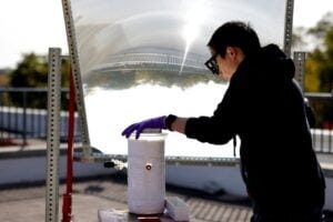 Peng Zhou uses a large lens to concentrate sunlight onto the water-splitting catalyst. Outdoors, the device was ten times more efficient than previous efforts at solar water splitting. Image credit: Brenda Ahearn/Michigan Engineering, Communications and Marketing