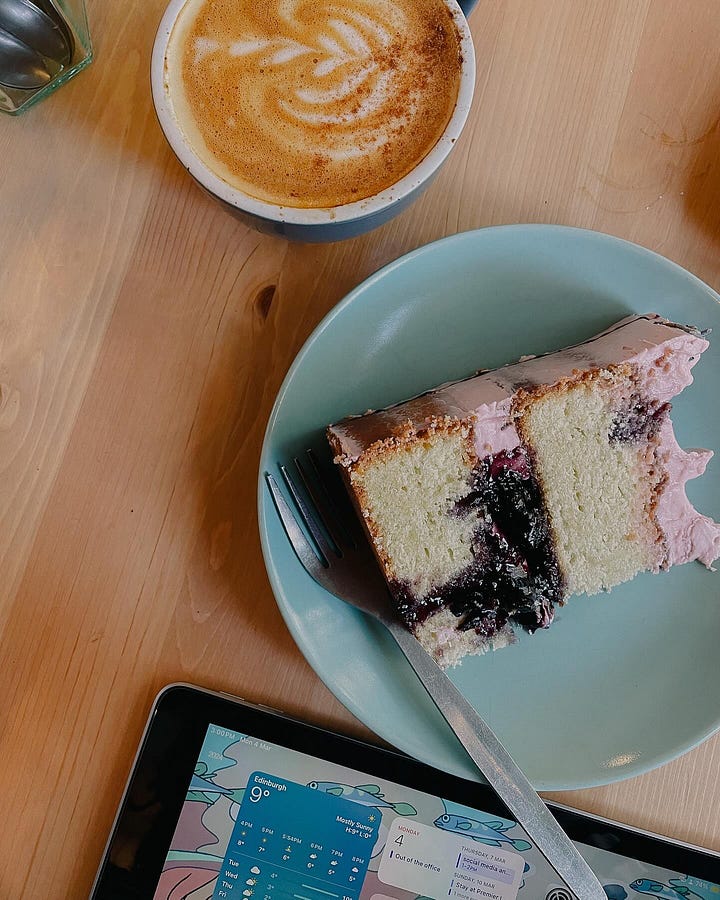 Image 1: Colourful café interior with a pink La Marzocco coffee machine, sage green walls, and plenty of plants. / Image 2: Overhead view of a dirty chai latte and a slice of lavender and blueberry cake.