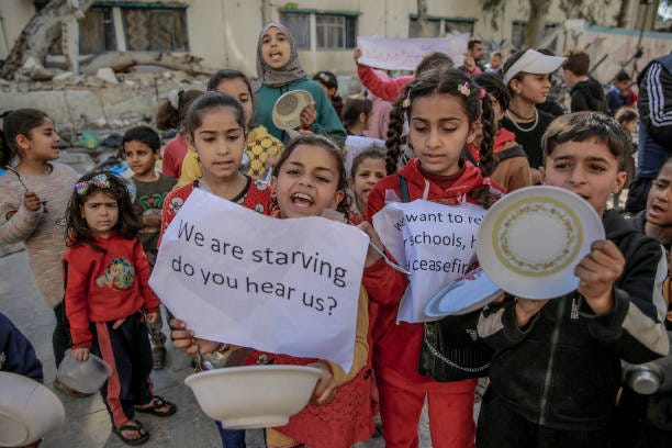 Palestinian children holding banners and empty bowls, gather to protest the food shortages in the city due to Israeli attacks and demanding a...