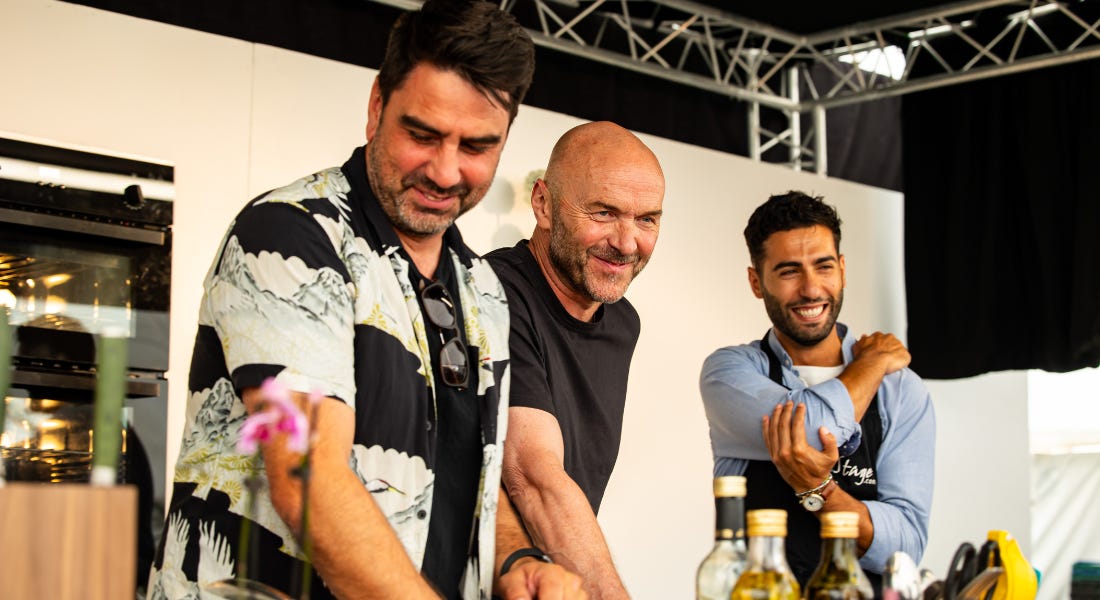 Three men stood on stage with two ovens behind them and oil bottles in front of them