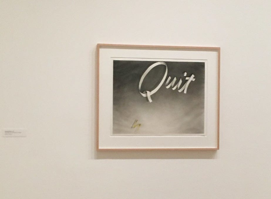 A black and white pencil drawing featuring the word QUIT, hanging in a frame at a museum.