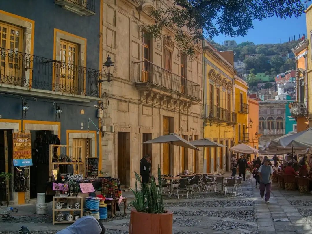 A row of grand buildings and a street filled with tables and chairs