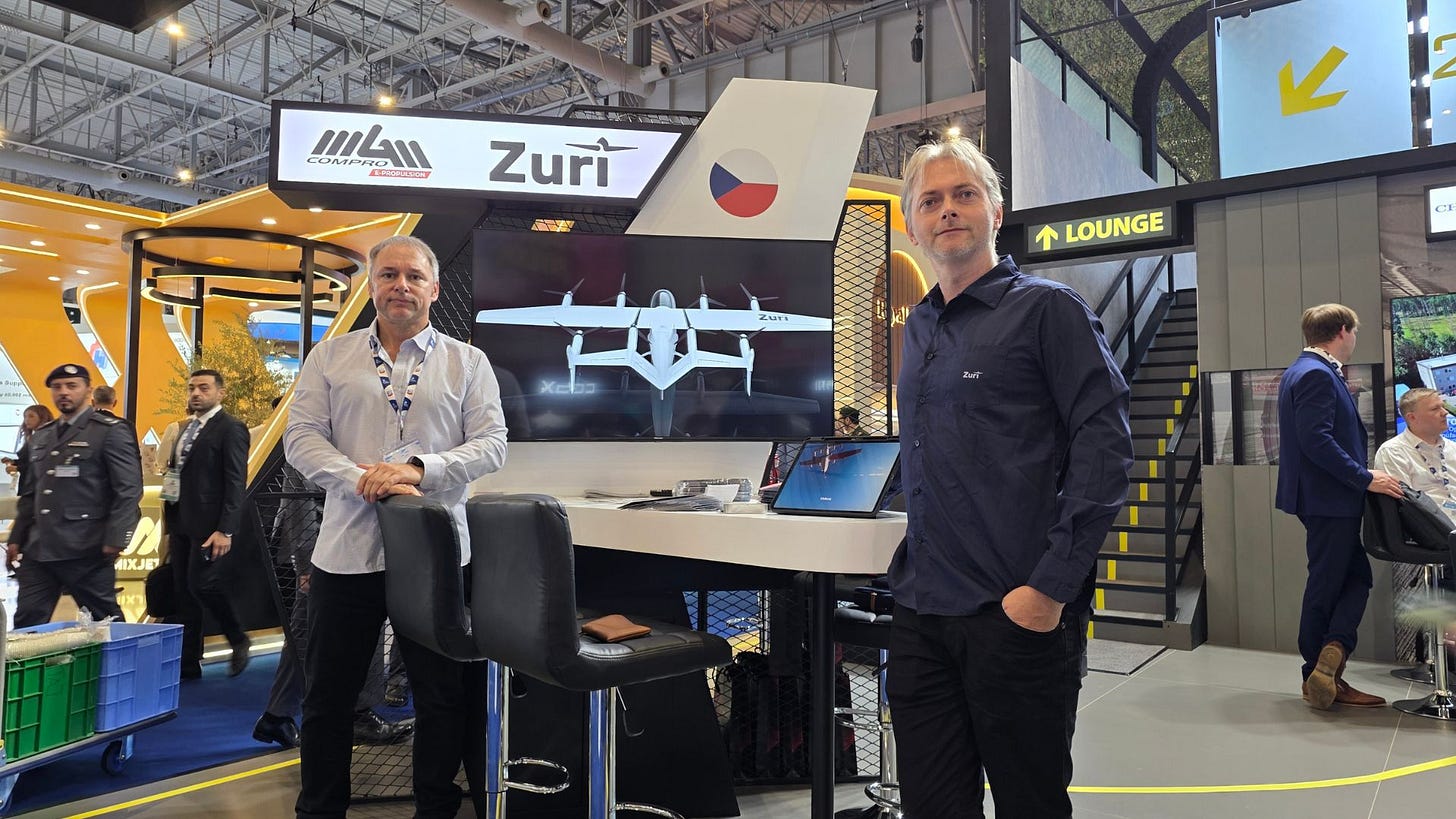 Zuri Hybrid VTOL team members standing at the Czech Republic Pavilion booth at Dubai Airshow 2025, with the aircraft concept displayed on the screen behind them. Zuri Hybrid VTOL team members standing at the Czech Republic Pavilion booth at Dubai Airshow 2025, with the aircraft concept displayed on the screen behind them.