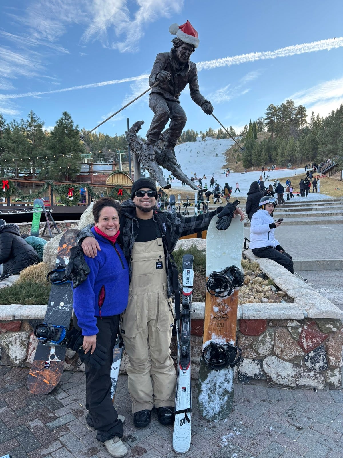 statue in front of mountain with ski slope and mom and son posing with skis and snowboard