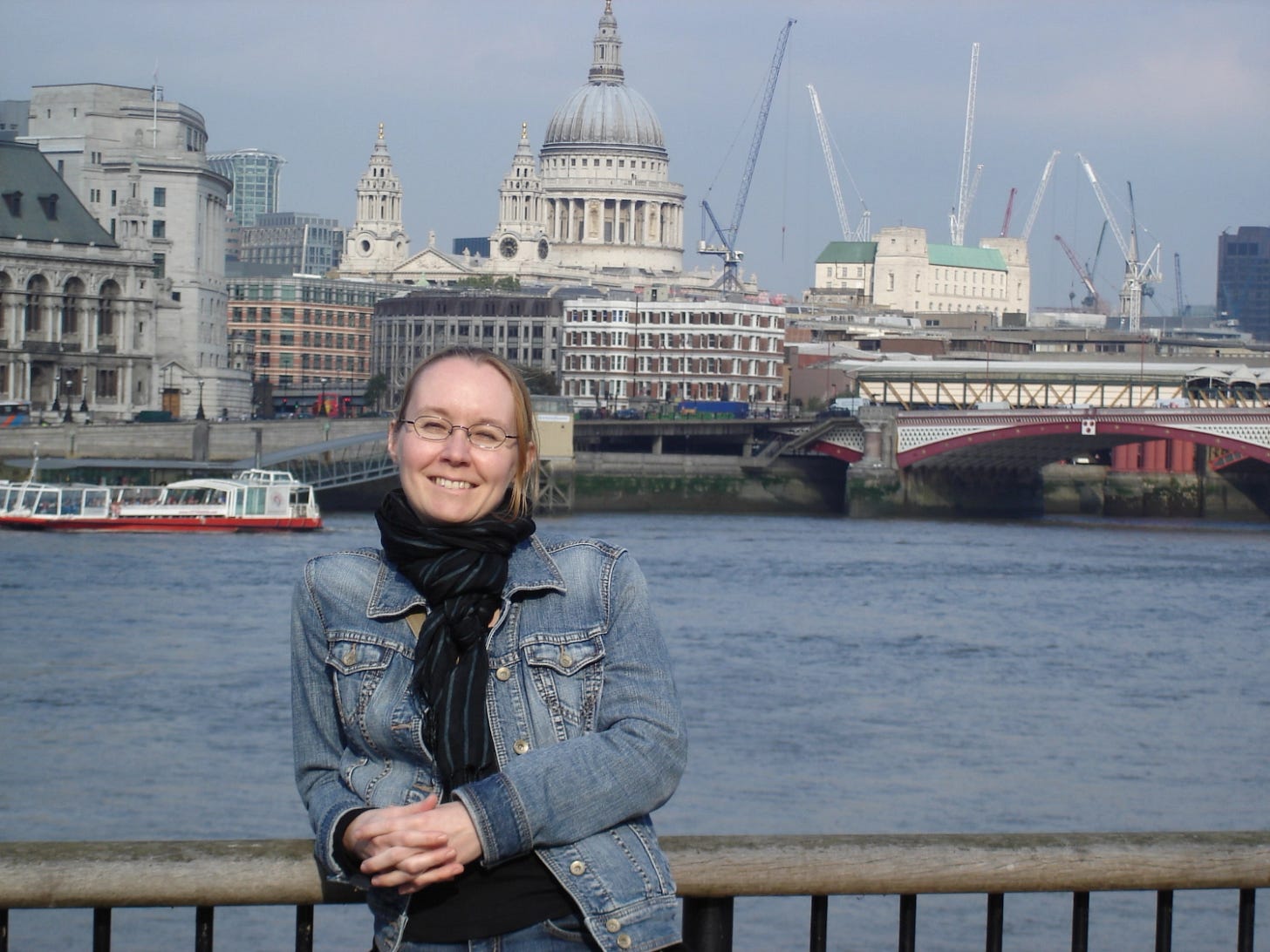 Claudia Kollschen in denim jacket stands on the bank of the Thames, St. Paul's cathedral in the back