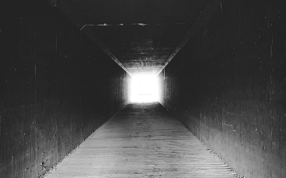 a black and white photo of a light at the end of a tunnel