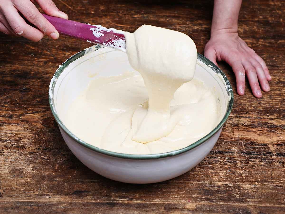 Tres leches cake mix dripping from spatula into bowl