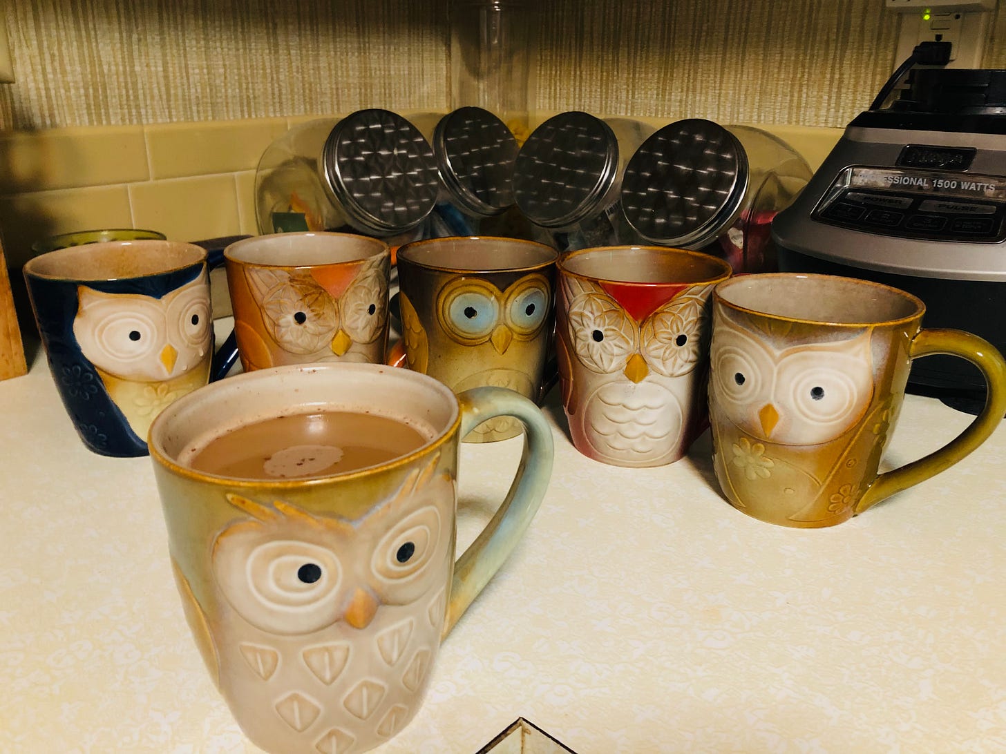 A set of owl mugs in varied color and expression, with the pale green and cream one filled with coffee