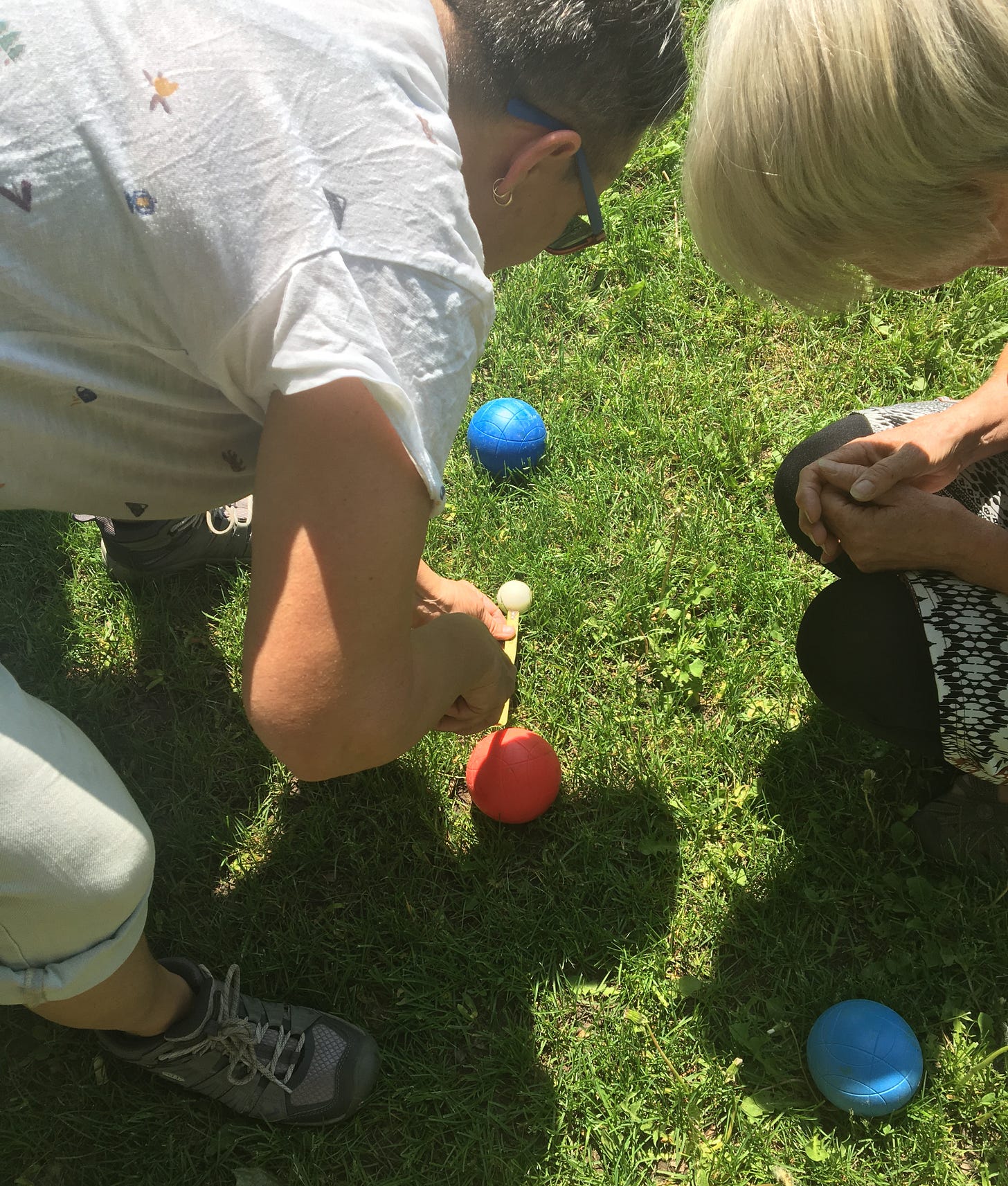 two women measuring bocce balls on the grass