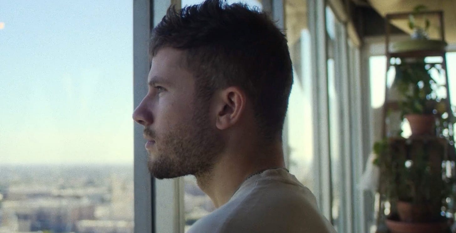 Travis Fountain in profile at a window over the Brooklyn skyline.