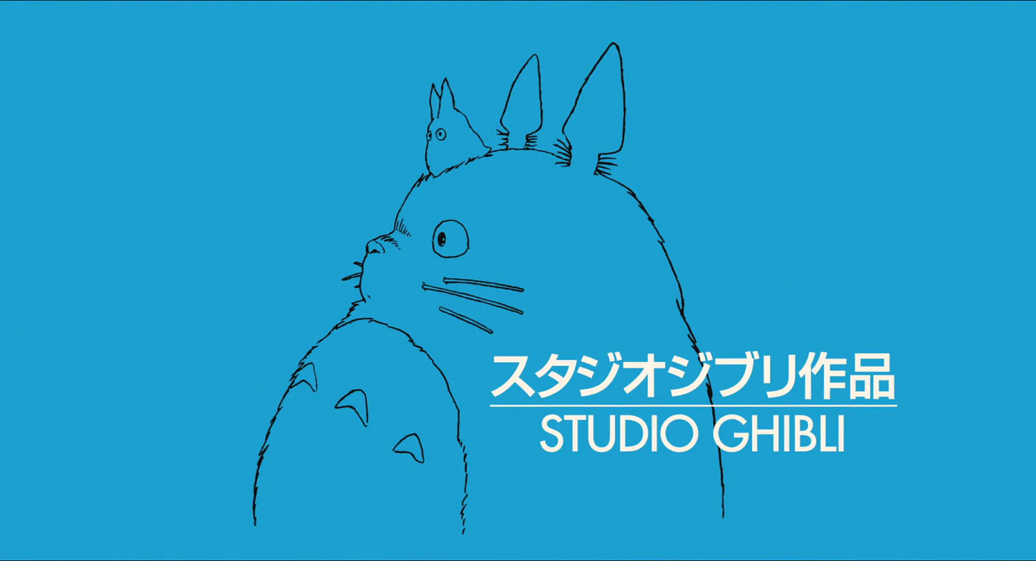 Logo do Studio Ghibli. Imagem com um fundo azul claro. Em branco, na parte direita inferior, escrito grande Studio Ghibli em inglês e em japonês, separados por uma linha. Desenhado ao fundo, em contorno preto, a imagem de Totoro e uma outra criatura da floresta: Totoro é um animal grande e peludo, como uma mistura de urso com gato. Ele tem orelhas pontudas, um corpo grande, redondo e peludo, grandes bigodes, um nariz pequeno e um contorno de barriga com três texturas como setas para cima. Em sua cabeça, o animal é pequeno, do tamanho da orelha. Ele é uma criatura com duas orelhas pontudas e dois olhos. Sem nenhum outro detalhe.