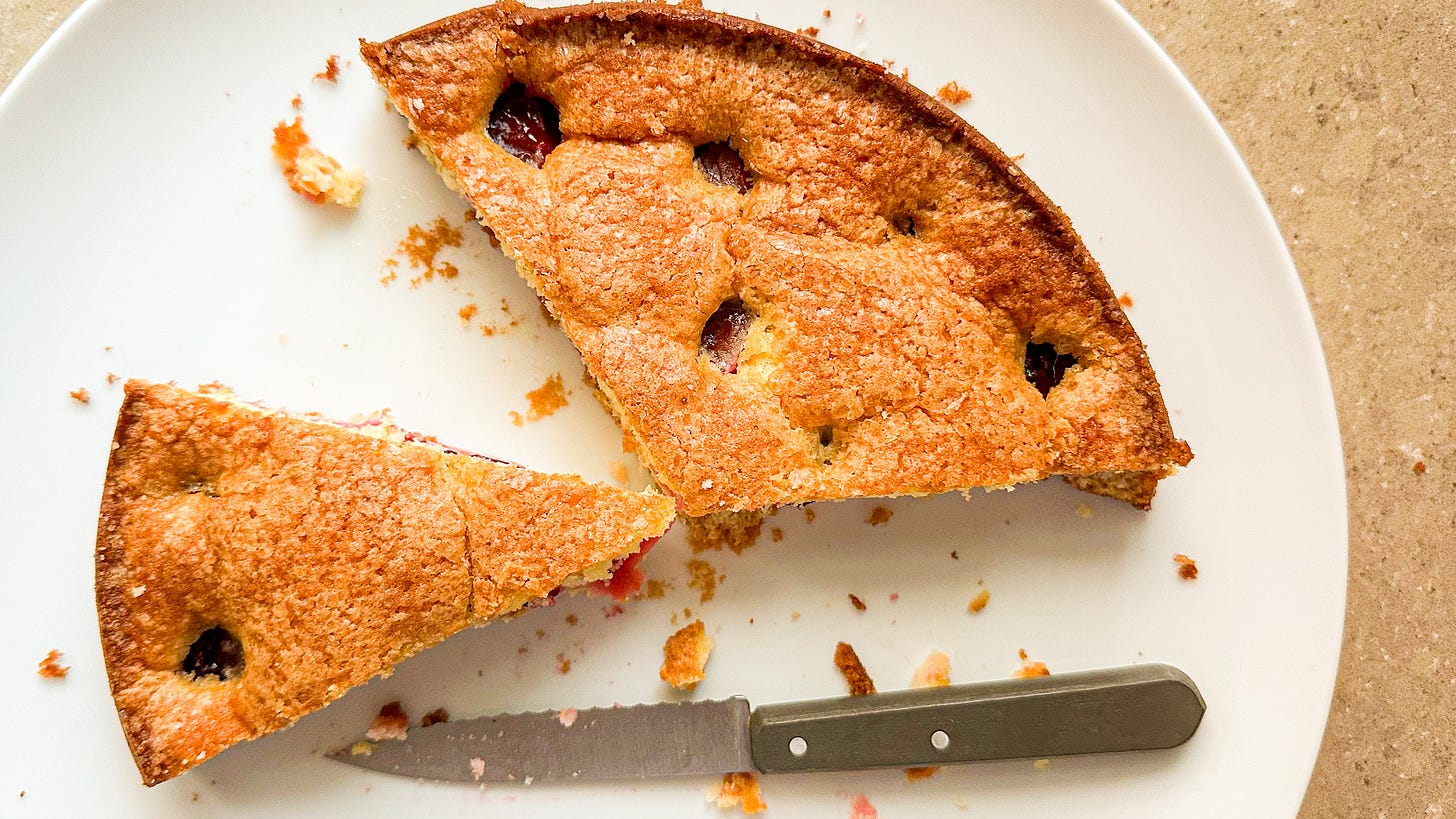 A golden brown plum torte cut into slices with a knife sitting on the plate.
