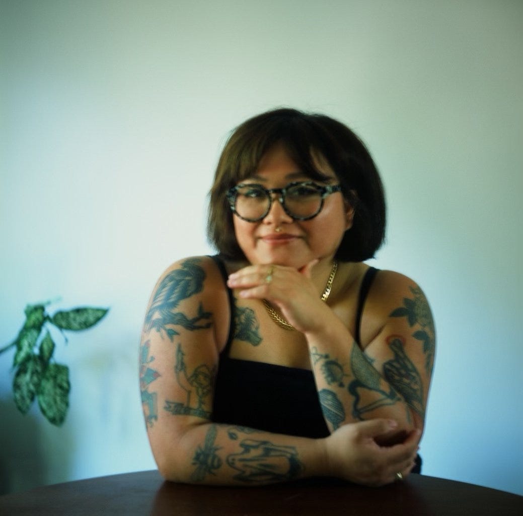 Author photo of Laura Chow Reeve, at home with a plant and some cool arm tats