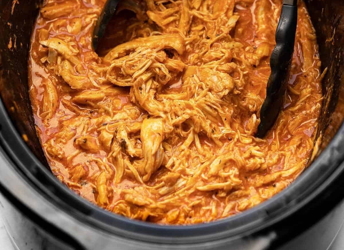 Shredded buffalo chicken in a slow cooker with tongs Shredded buffalo chicken in a slow cooker with tongs