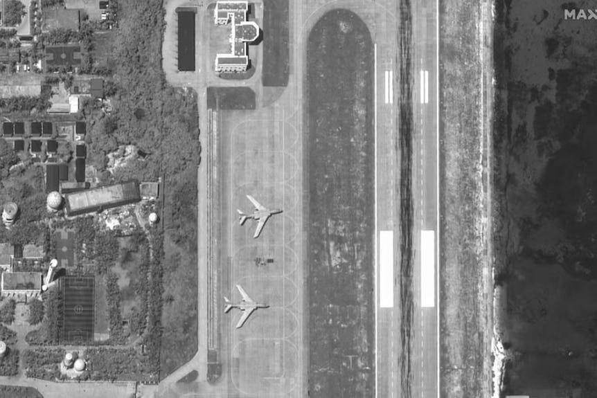 A black-and-white satellite photo of two large bombers parked on a runway.