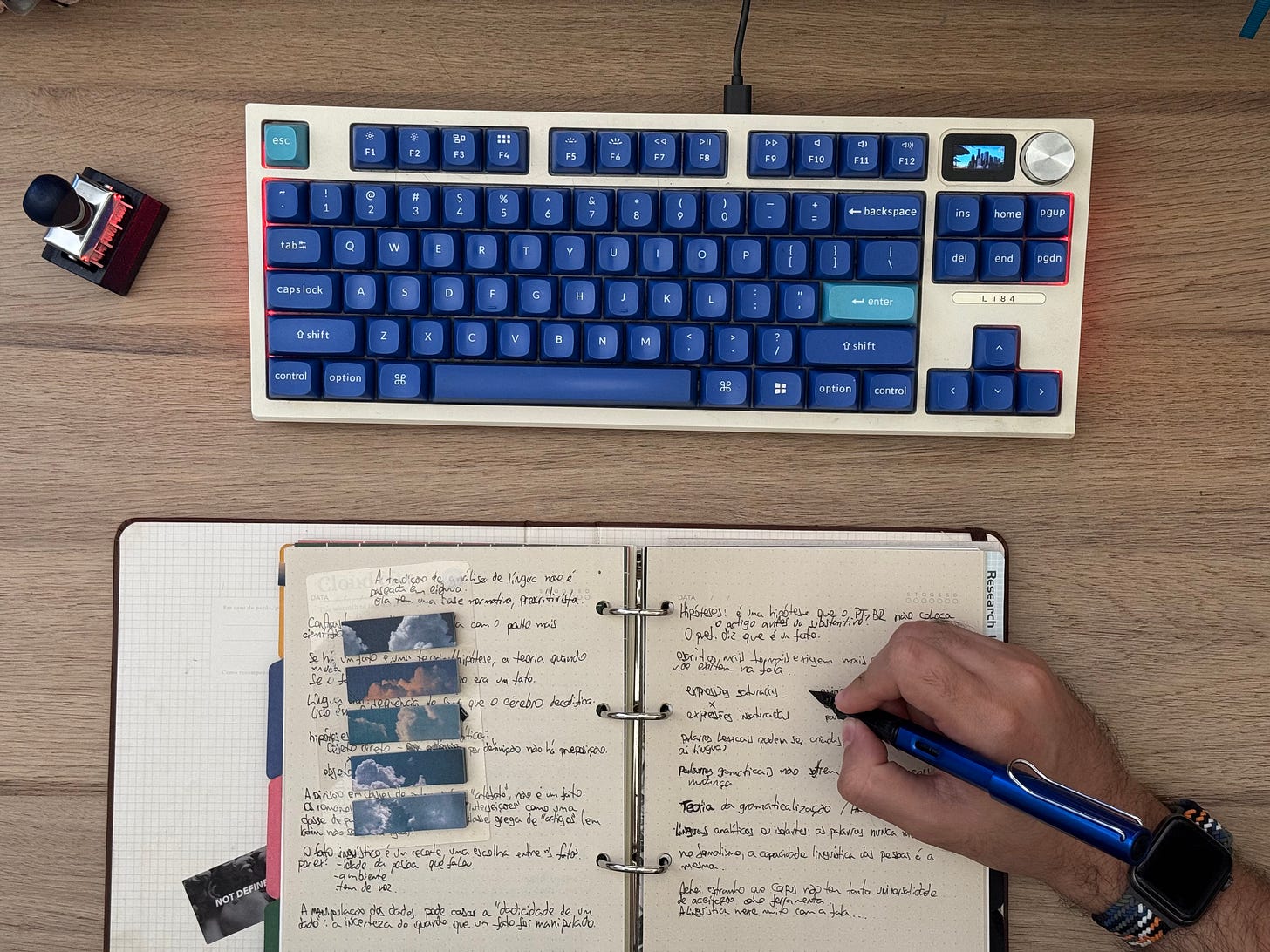 Teclado de computador com teclas azuis e um fichário sobre uma mesa, com uma mão segurando uma caneta tinteiro azul para fazer anotações Teclado de computador com teclas azuis e um fichário sobre uma mesa, com uma mão segurando uma caneta tinteiro azul para fazer anotações
