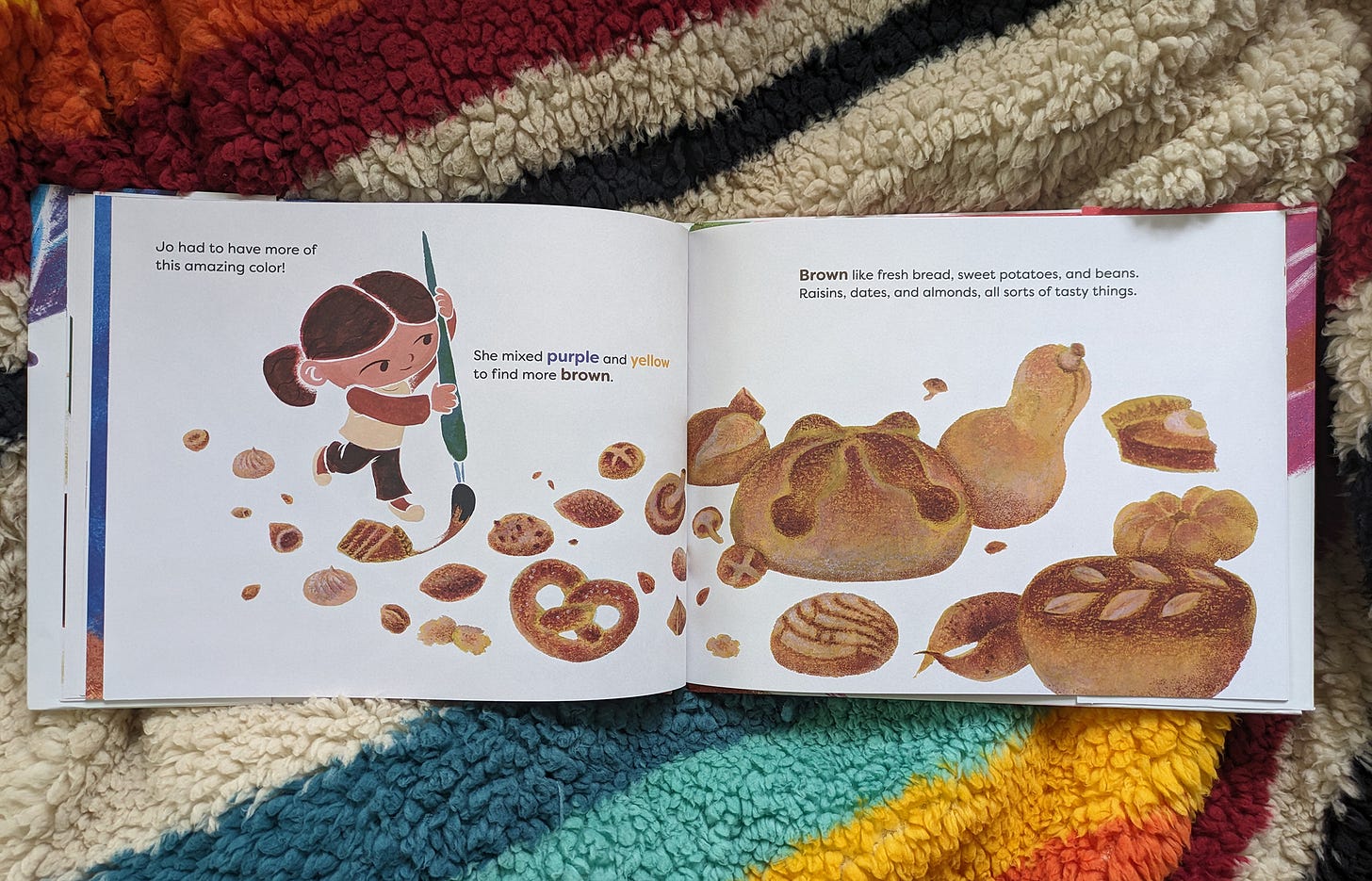 The picture book A RAINBOW IN BROWN atop a rainbow-colored blanket, open to an interior spread