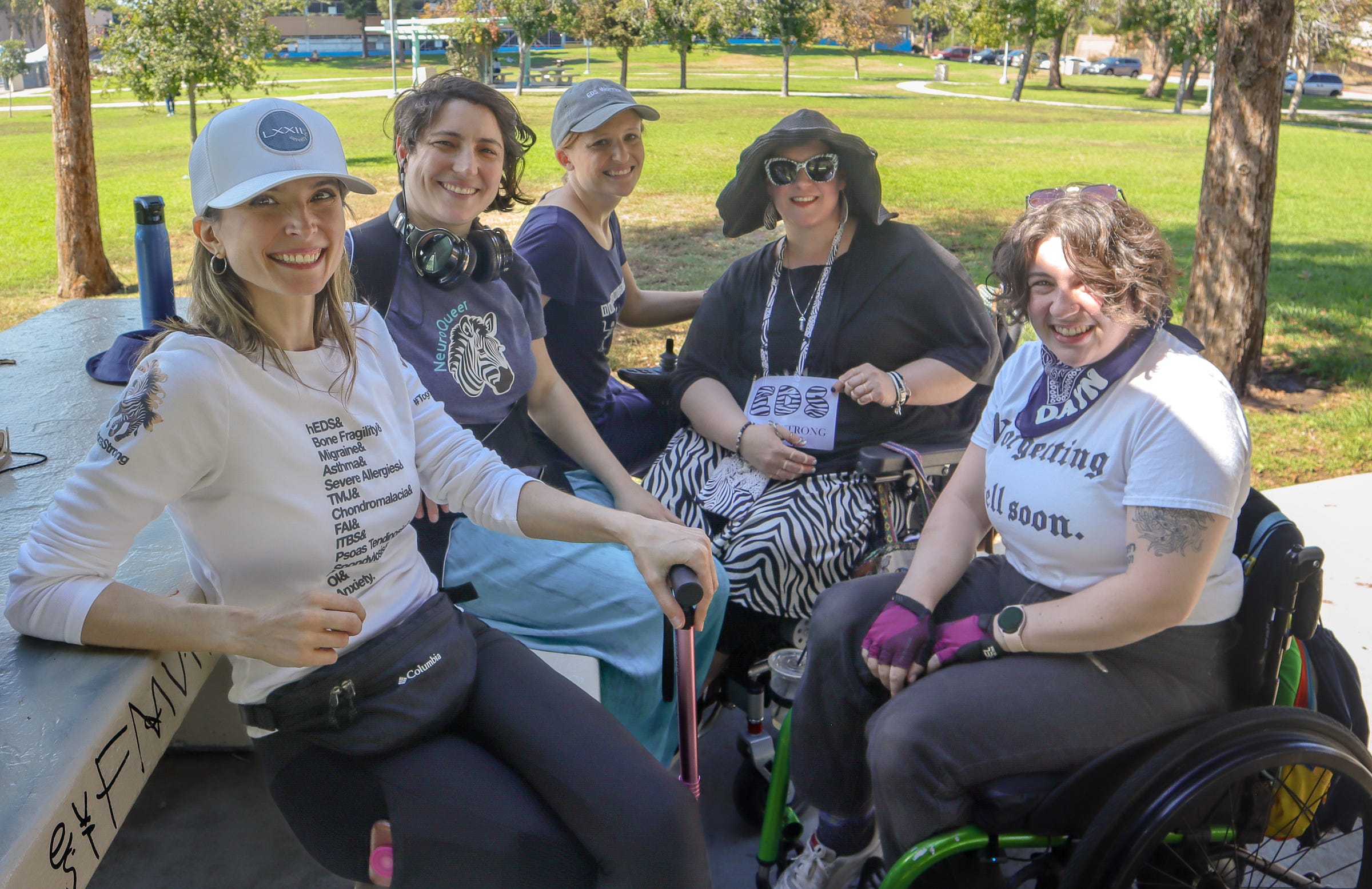 Five women wearing zebra themed clothing with a park behind them smile at the camera