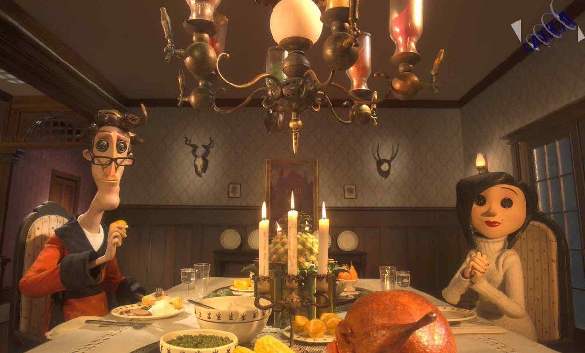 Stop-motion figures sit at a dining table laden with food and decorated with candles. They have buttons for eyes. 