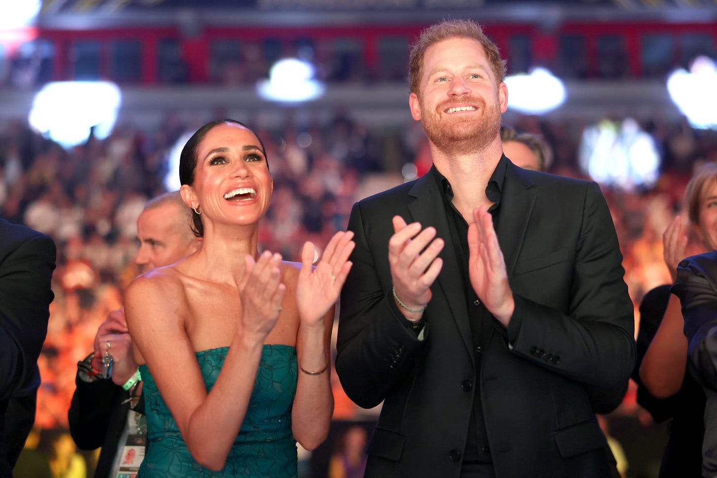 Prince Harry and Meghan Markle standing up smiling and clapping