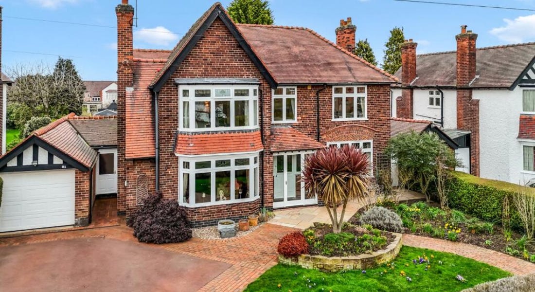 A large brick house with white windows, a lawn, and driveway in front of it