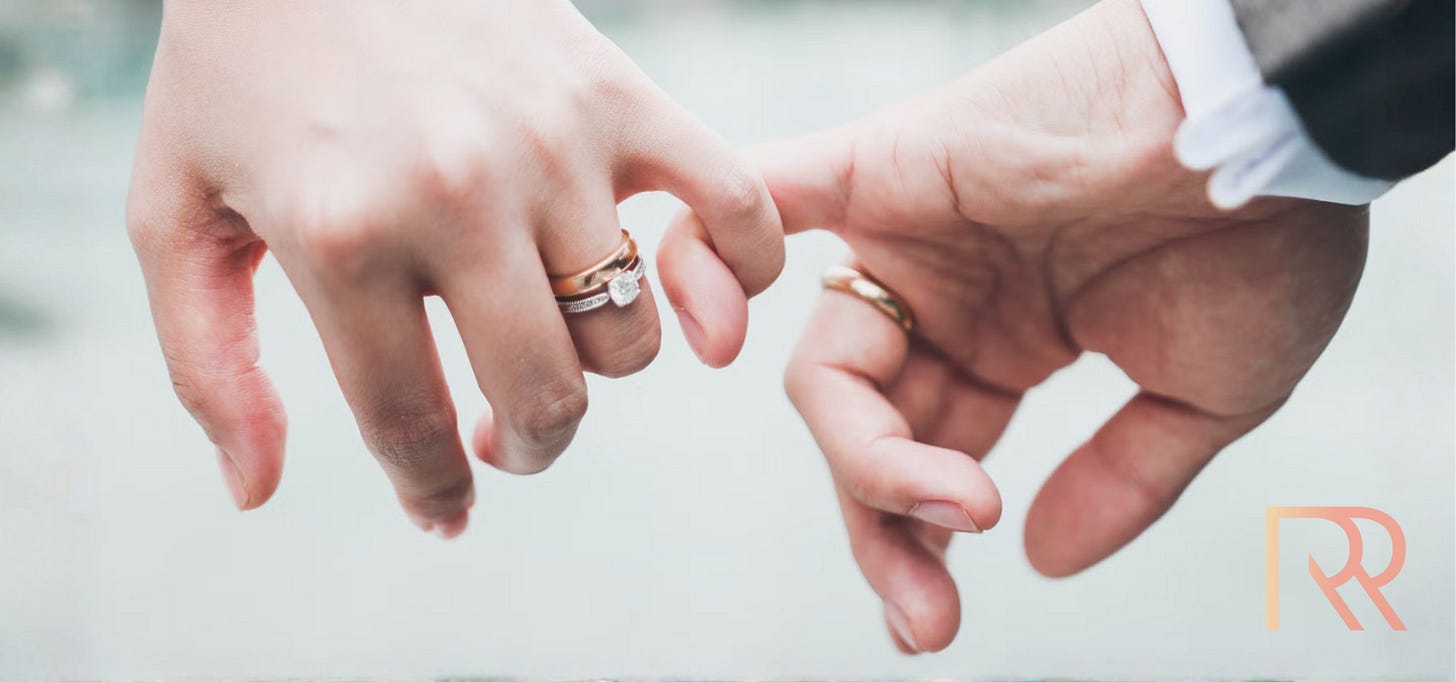 Close-up van twee handen met trouwringen die elkaar zacht aanraken en de pinken in elkaar haken, als symbool van liefde en verbondenheid. De achtergrond is zacht vervaagd. Close-up van twee handen met trouwringen die elkaar zacht aanraken en de pinken in elkaar haken, als symbool van liefde en verbondenheid. De achtergrond is zacht vervaagd.