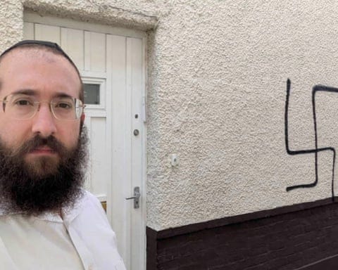 Bentzion Alperowitz standing alongside the swastika graffito on the wall of his house