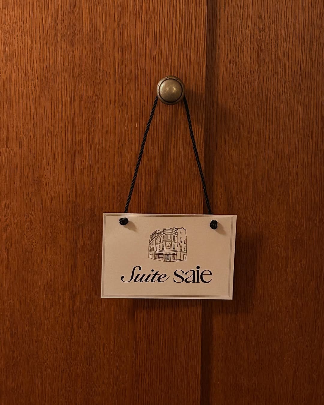 A sign that reads "Suite Saie" hanging on a wooden door.