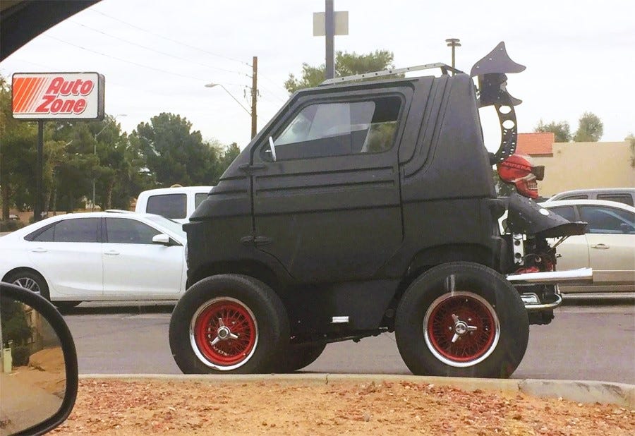 Photo of a highly modified black micro car with huge wheels, 'Mad Max' style accessories, including a fake skull that's painted red and wearing offroad goggles Photo of a highly modified black micro car with huge wheels, 'Mad Max' style accessories, including a fake skull that's painted red and wearing offroad goggles