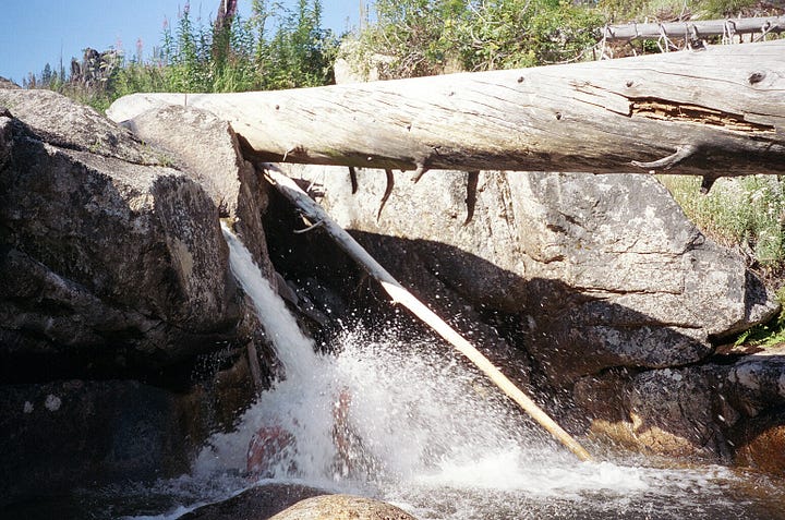 Two men on a mountaintop, a bridge over a creek, a backpack with tools, a waterfall.