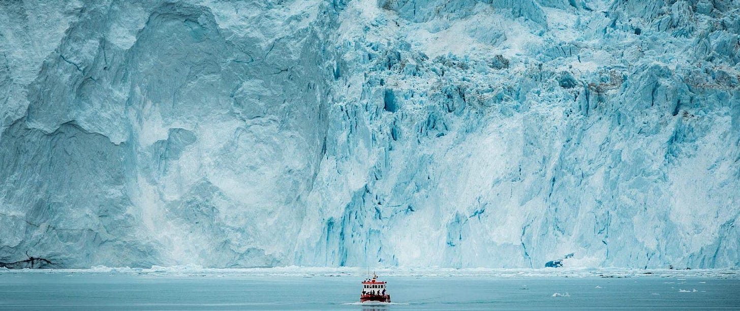 A small passenger boat in front of the huge glacier wall at the Eqi glacier in Greenland. Photo by Mads Pihl