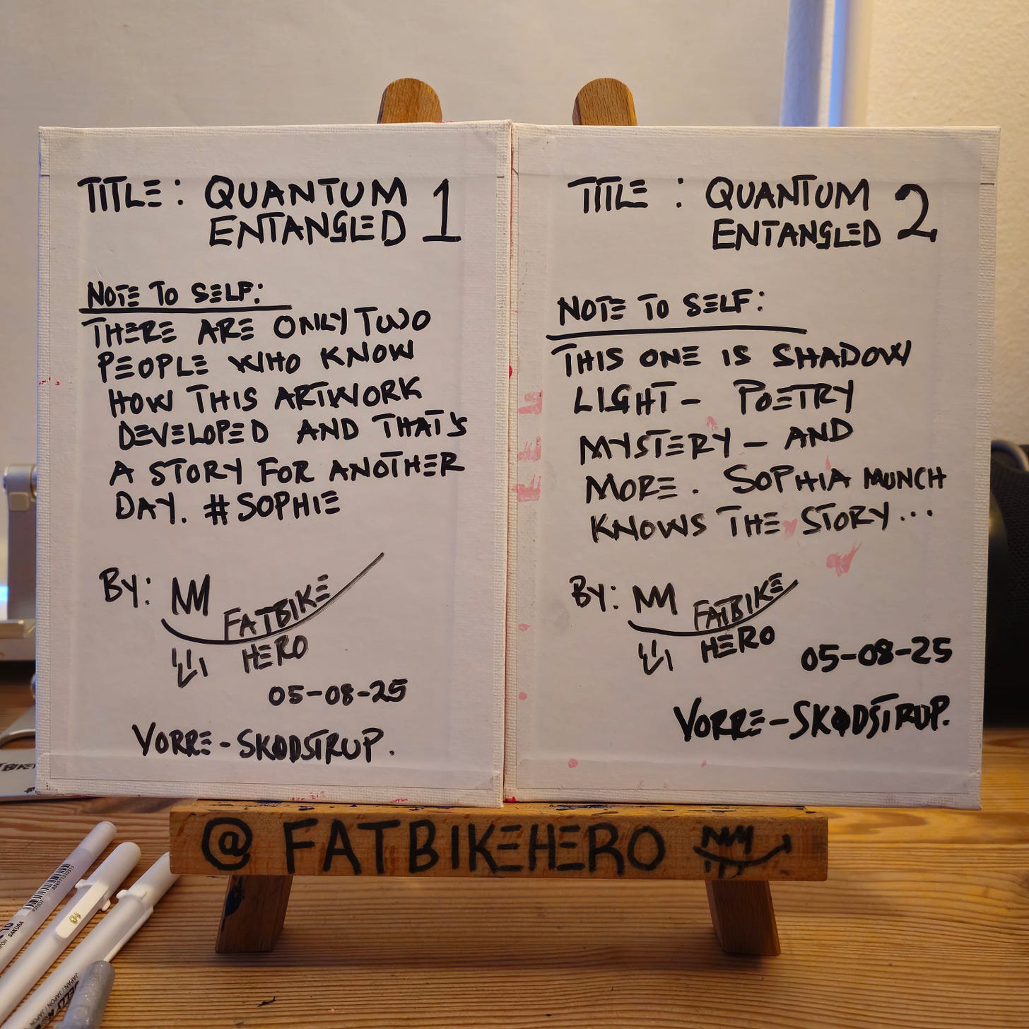 Alt Text: The reverse side of two canvases. Handwritten text in black marker reads "TITLE: QUANTUM ENTANGLED" and includes notes about a secret story involving "Sophia Munch," signed by FatbikeHero, dated 05-08-25, Vorre-Skodstrup.