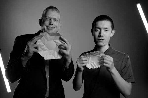 Larry Howell and Kelvin Wang hold up unfolded bloom pattern origami papers.