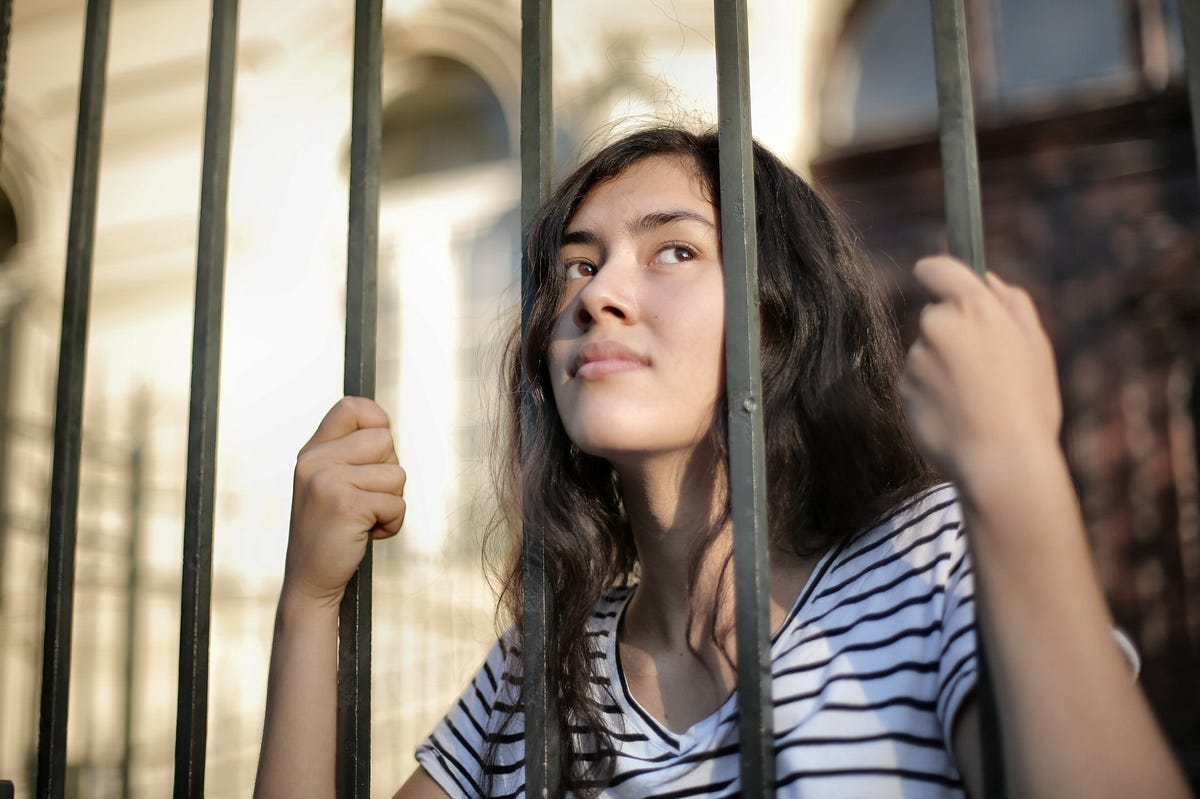 Young woman grabbing “jail bars” with her head between 2 bars