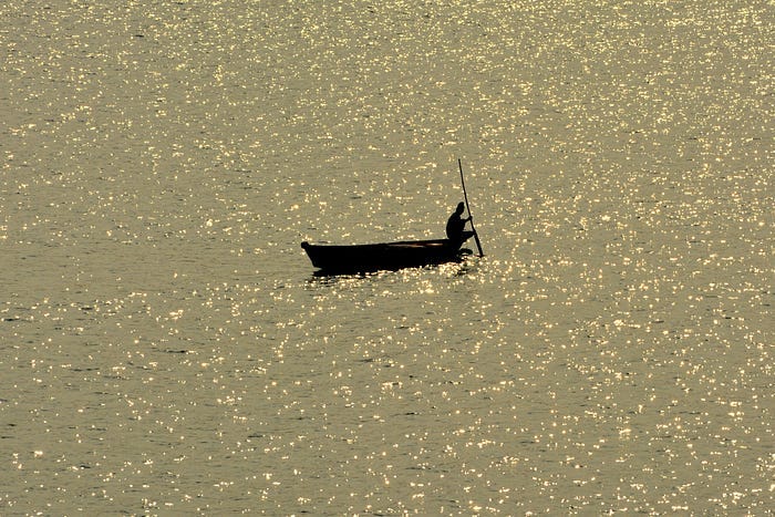 A person in a boat, silhouetted against a golden glittering ocean