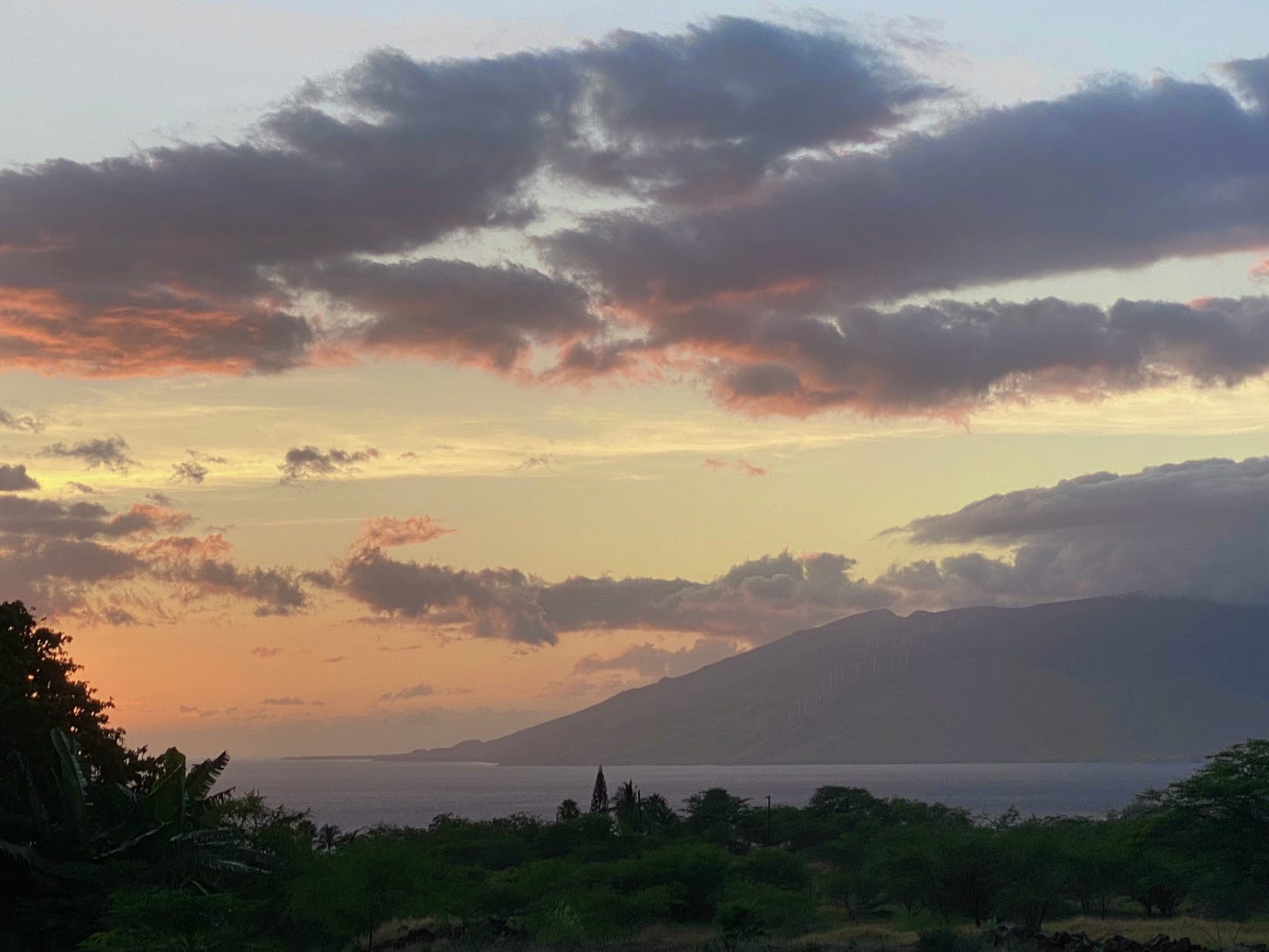 The same mountain and bay in sunset light, with fluffy gray clouds tinged red and water of blue-violet.