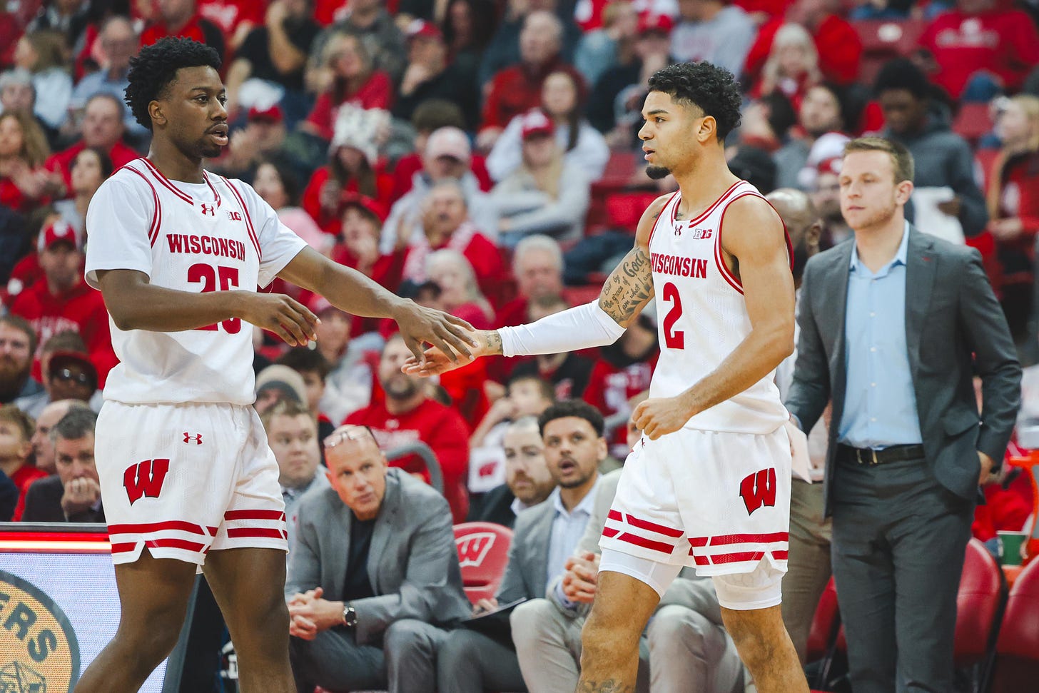 Badgers basketball guards John Blackwell and Nick Boyd in white home jerseys each with one hand outstretched to the other person