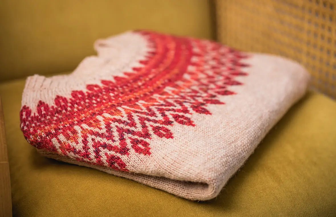 beige sweater with red colorwork yoke on a mustard colored sofa