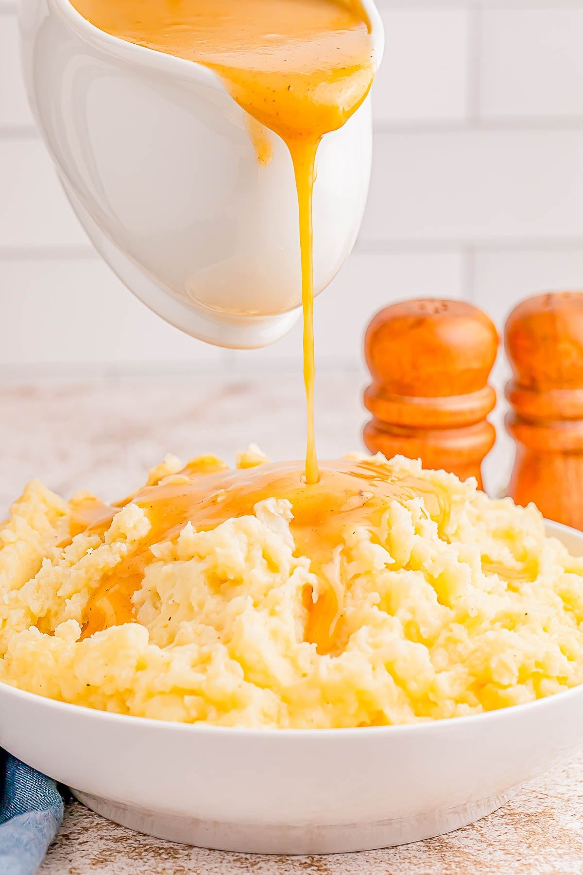 Gravy being poured over a bowl of mashed potatoes, with salt and pepper shakers in the background. Gravy being poured over a bowl of mashed potatoes, with salt and pepper shakers in the background.
