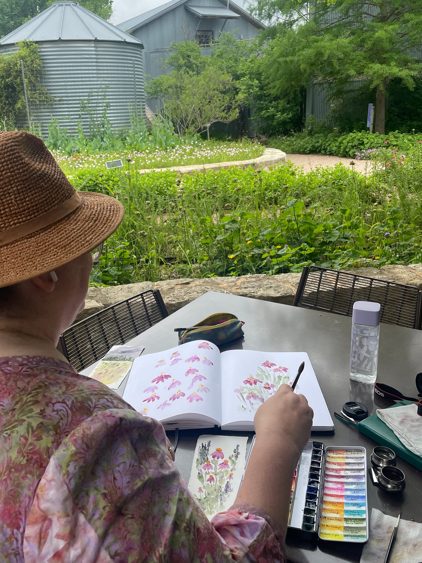 Woman in straw hat painting purple coneflowers outdoors with watercolors on paper Woman in straw hat painting purple coneflowers outdoors with watercolors on paper