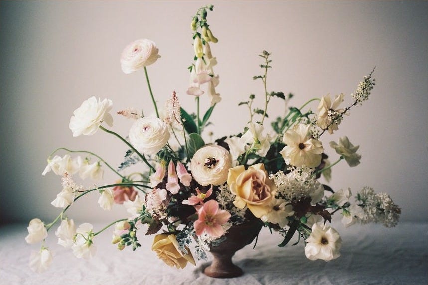 May include: A framed photograph of a floral arrangement in a brown vase. The arrangement features white, pink, and yellow flowers, including roses, lilies, and other blooms. The background is a light gray wall.