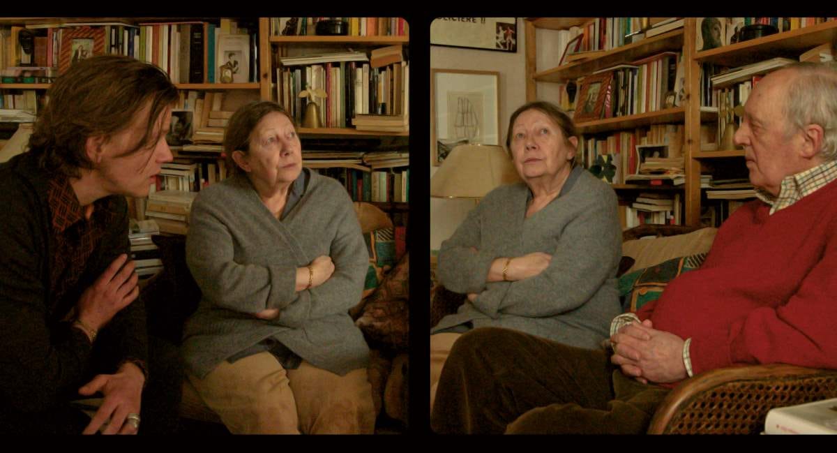 Cena do filme Vortex, dividida em dois quadros. No primeiro, uma senhora de casaco, sentada de braços cruzados ao lado de um homem jovem. No segundo quadro, a mesma senhora, na mesma posição, e sentado do outro lado dela um senhor de suéter vermelho. Atrás deles, uma estante abarrotada de livros Cena do filme Vortex, dividida em dois quadros. No primeiro, uma senhora de casaco, sentada de braços cruzados ao lado de um homem jovem. No segundo quadro, a mesma senhora, na mesma posição, e sentado do outro lado dela um senhor de suéter vermelho. Atrás deles, uma estante abarrotada de livros