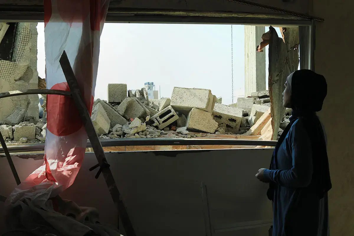 A woman looks out at rubble from inside a ruined building.