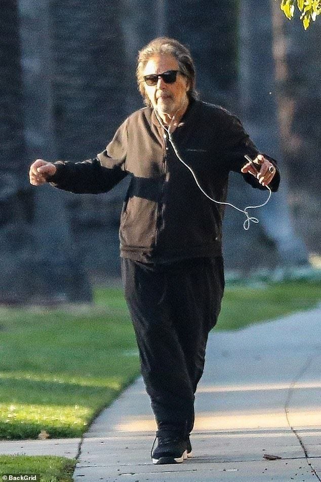 This may contain: an older man walking down a sidewalk while listening to headphones