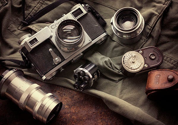 camera fotográfica Contax II usada por Robert Capa, junto de outras lentes e fotômetros antigos, repousam em uam mesa